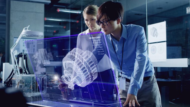 Two people in a modern office closely examine a large, futuristic transparent display showing a 3D holographic model of a mechanical component, likely an engine or motor, with technical diagrams in the background.