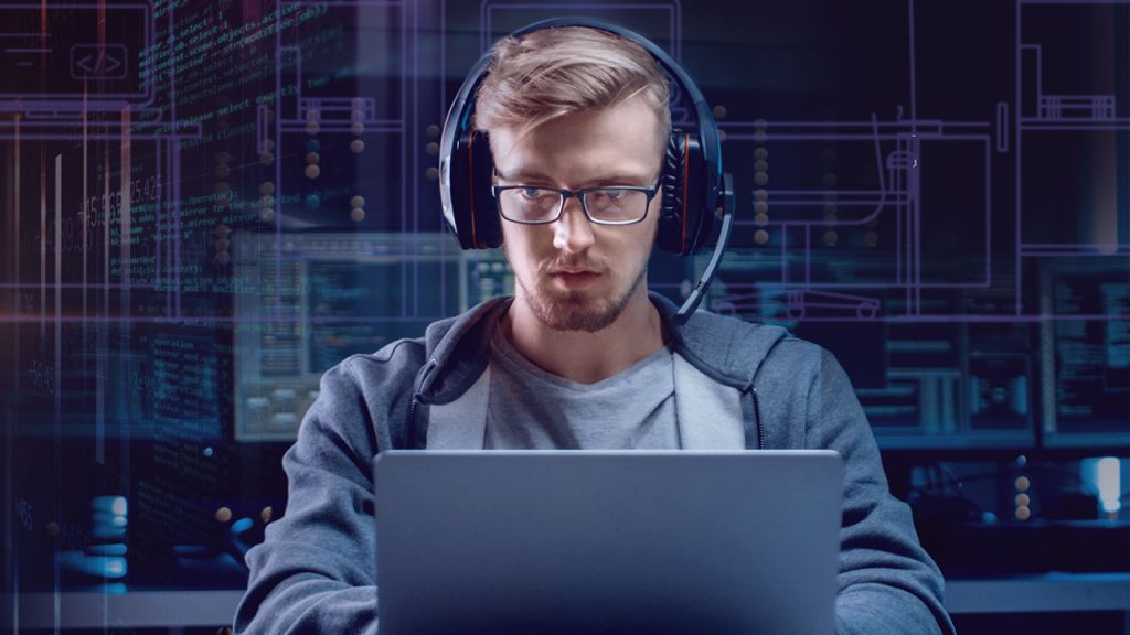 A man wearing glasses and headphones is intensely focused on his laptop in a dimly lit room. The background features complex computer code and technical diagrams, giving the scene a high-tech, coding environment vibe.