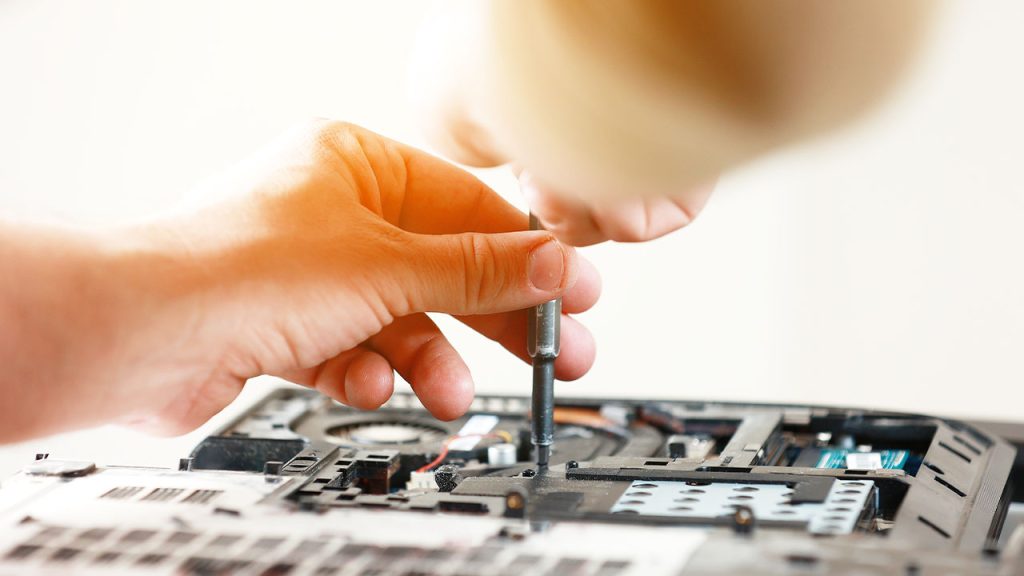 A person is using a screwdriver to repair or assemble a laptop. The focus is on their hands holding the tool and working on the internal components of the laptop, which is placed on a surface.