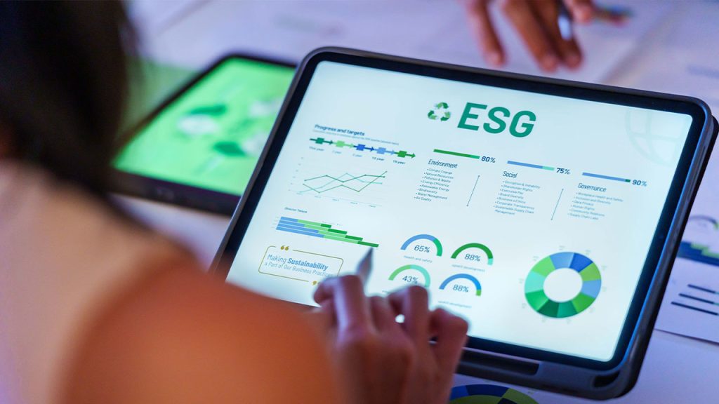 A person is interacting with a tablet displaying ESG (Environmental, Social, and Governance) data, including graphs, charts, and progress indicators. The screen shows circular graphs and percentages for different ESG categories.