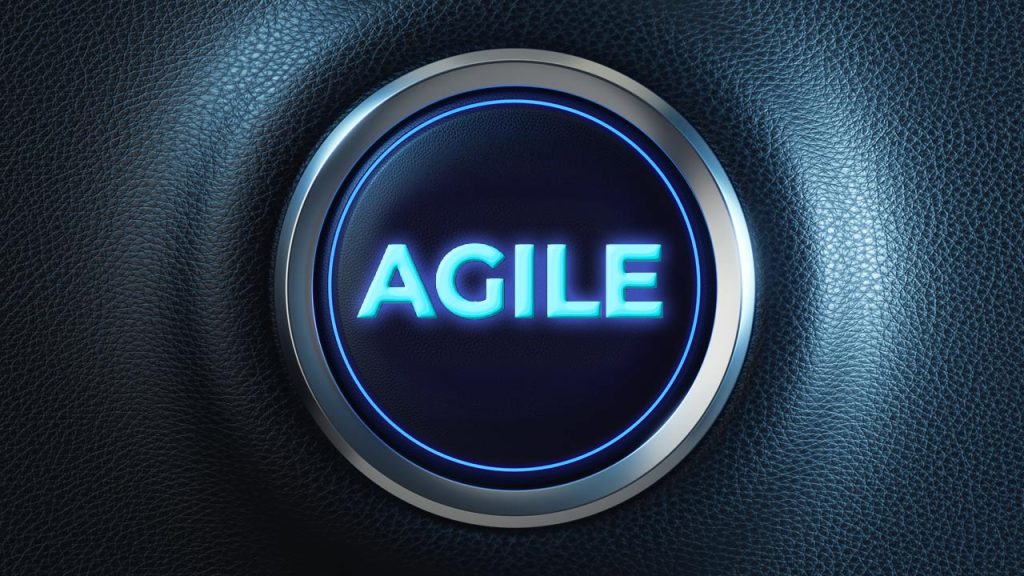 Illuminated circular button with the word "AGILE" in glowing blue letters in the center, set against a textured dark background. The button resembles a modern, high-tech interface element.