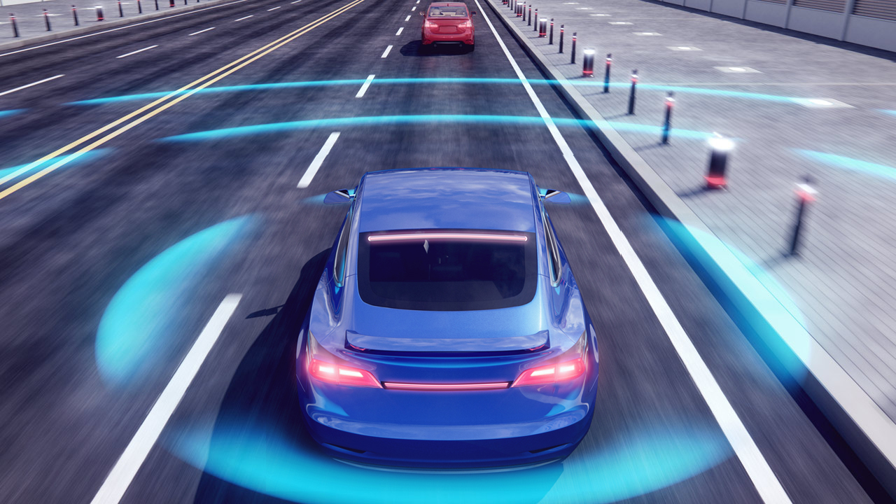 A blue car driving on a road with digital blue waves around it, illustrating autonomous or self-driving technology. Another car is visible ahead, and traffic cones line the right side of the street.