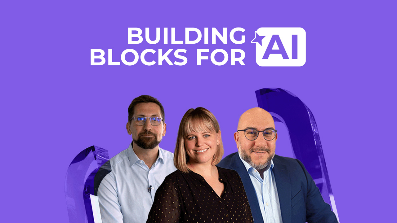 Three people stand in front of a purple background with the text “Building Blocks for AI.” Two men, one with glasses and a beard, and a woman with blonde hair, are smiling at the camera.