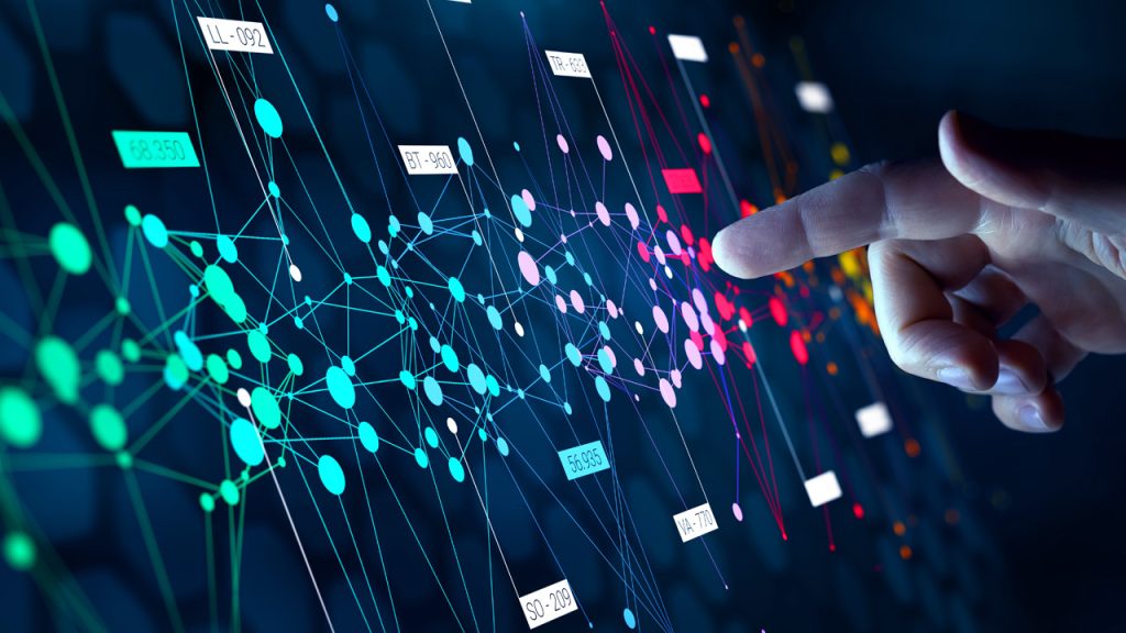 A hand points to a digital screen displaying a colorful network of interconnected nodes, lines, and data points, representing data analysis or artificial intelligence visualization.