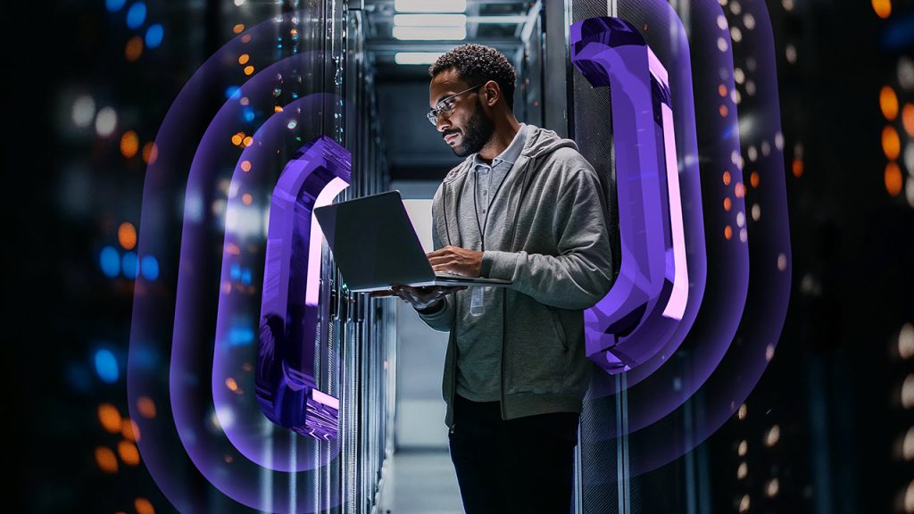 A person stands in a server room working on a laptop, surrounded by glowing, stylized purple digital shapes, suggesting technology, cybersecurity, or data processing concepts.