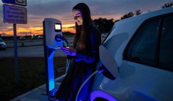A woman charging an electric car and looking at her phone