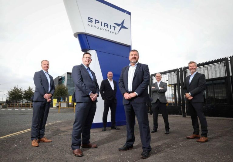 Men in suits stand in front of a banner with the Spirt Aerosystems logo