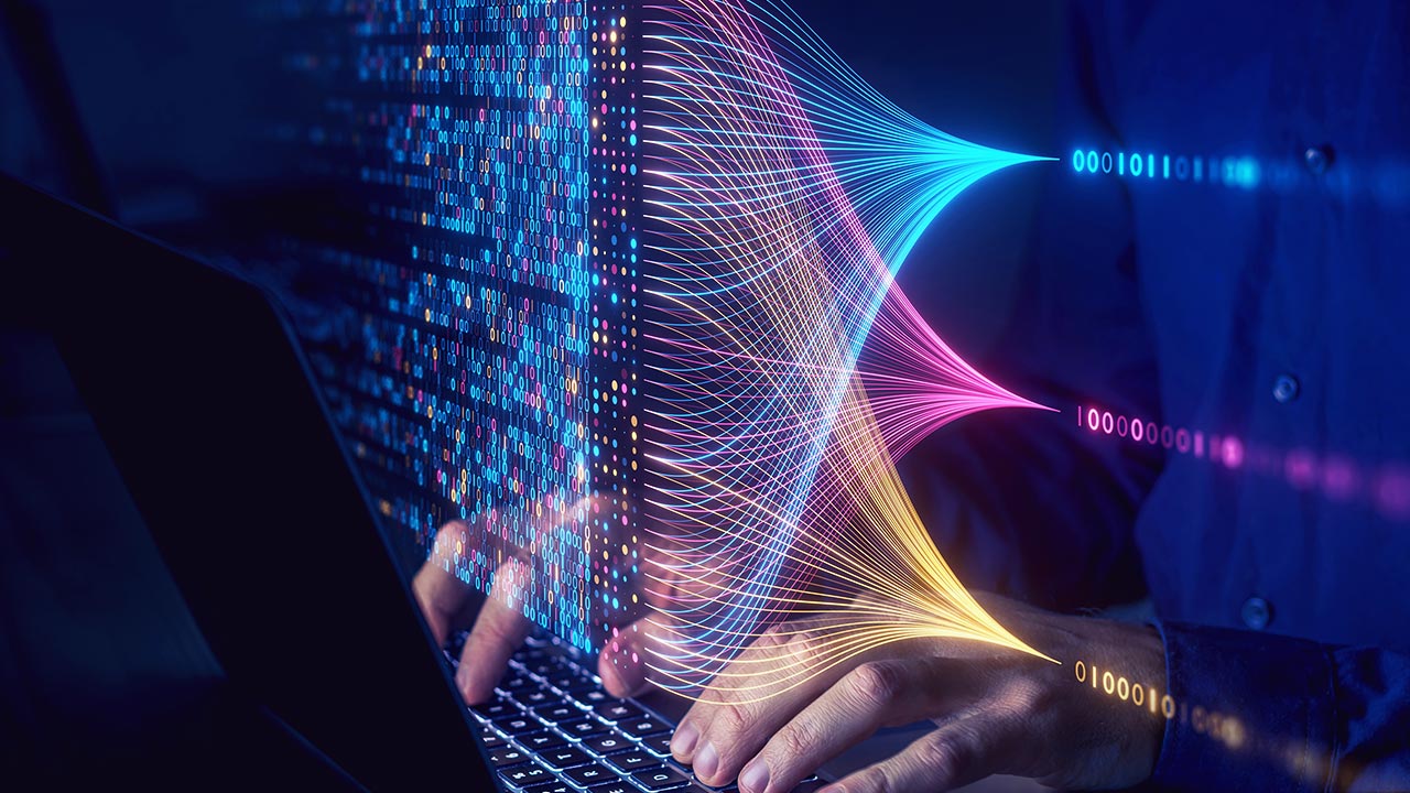 Hands typing on a laptop with colourful digital lines, binary code, and data patterns flowing from the screen, symbolising data processing, coding, or artificial intelligence technology.