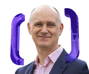 A smiling bald man in a suit and pink shirt stands in front of large purple brackets on a white background.