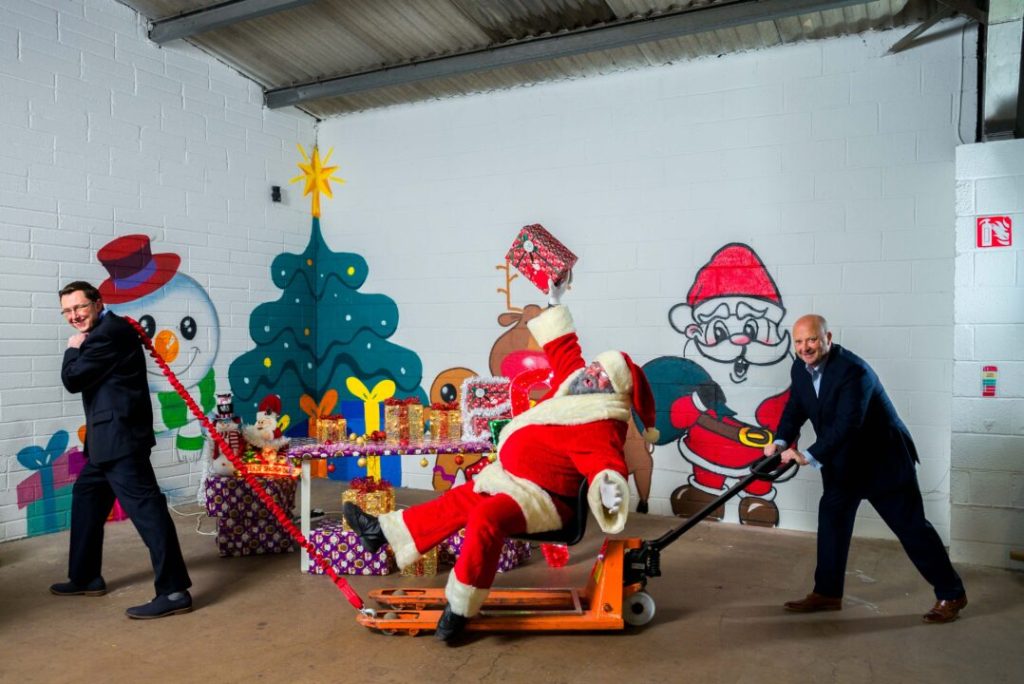 Two men pull Santa Claus sitting in a chair
