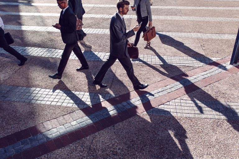 Businessmen, staring at their smartphones, are crossing the pedestrian crossing.