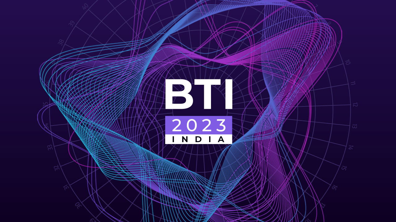 Abstract purple background with intertwined light pink and blue lines forming a dynamic shape, featuring the text "bti 2023 india" in white, centered.