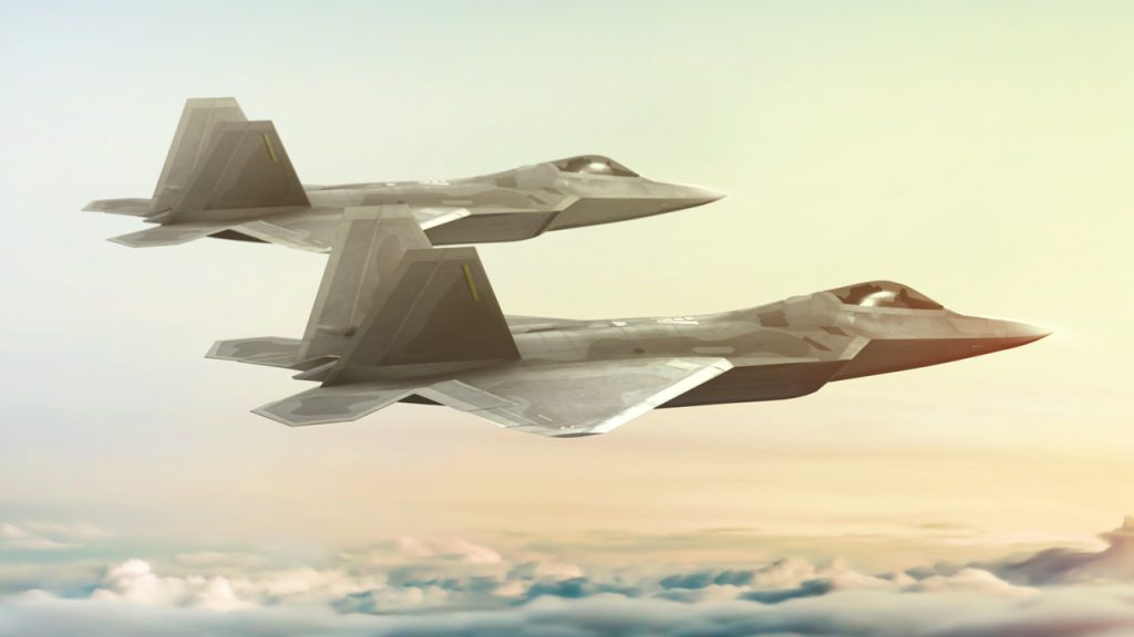 Two modern stealth fighter jets fly in formation above the clouds with a soft, pastel sky in the background.