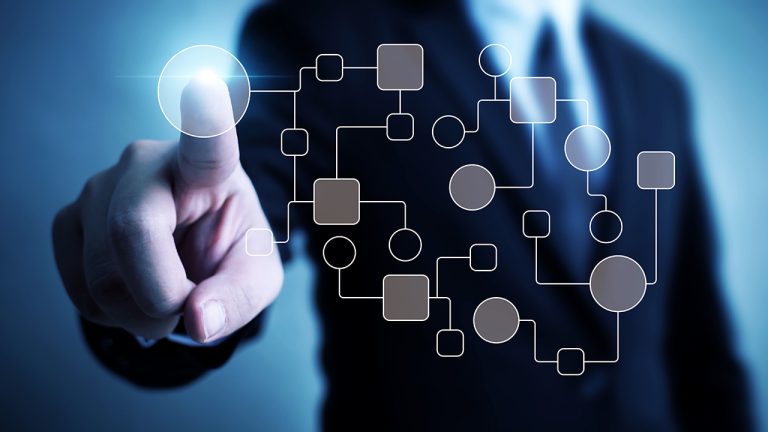 A person in a business suit is pressing a translucent touch screen. The screen displays an abstract network of interconnected squares and circles, symbolizing technology, connectivity, or data flow. The background is blurred, focusing on the finger and the screen.