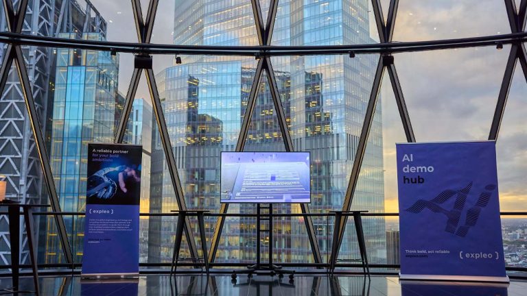 A modern office space with large glass windows overlooking city skyscrapers at sunset. In the foreground, there's a screen displaying digital content and two banners: one reading "A reliable partner for your" and the other "AI demo hub.