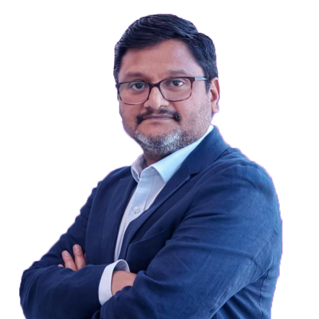 A man with glasses and a beard, wearing a navy blue suit and white shirt, stands with arms folded against a plain white background.