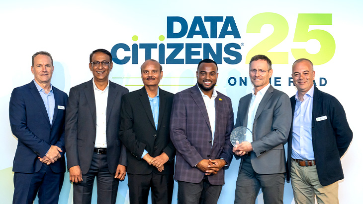 Six men in business attire stand and smile in front of a "DATA CITIZENS 25" event backdrop; one man holds a glass award.