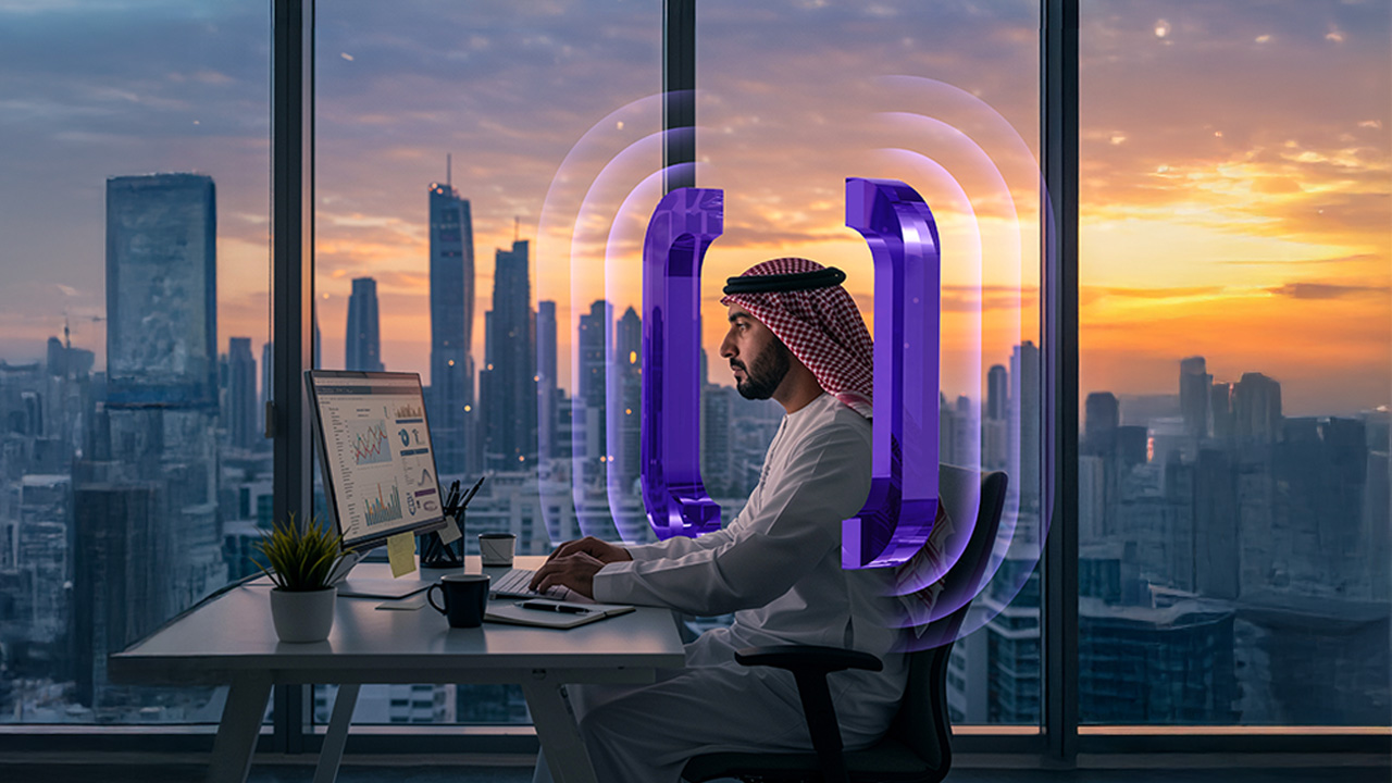 A man in traditional Middle Eastern attire works at a computer in a modern office with large windows overlooking a city skyline at sunset. Purple digital graphics surround him, symbolizing technology or connectivity.