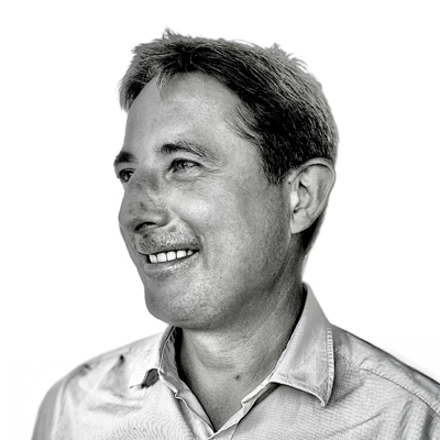 Black and white portrait of a man with short hair, smiling and looking to the left. He is wearing a light-coloured collared shirt and the background is plain white.