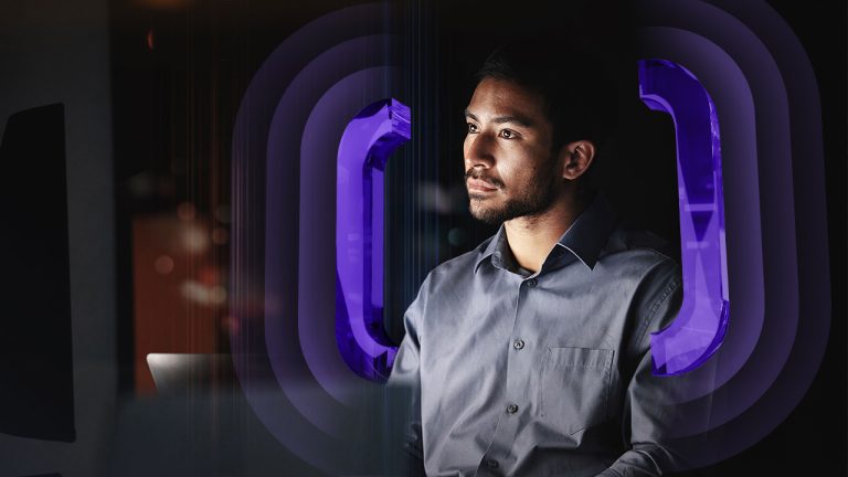 A man in a buttoned-down shirt looks at a computer screen surrounded by glowing purple brackets.