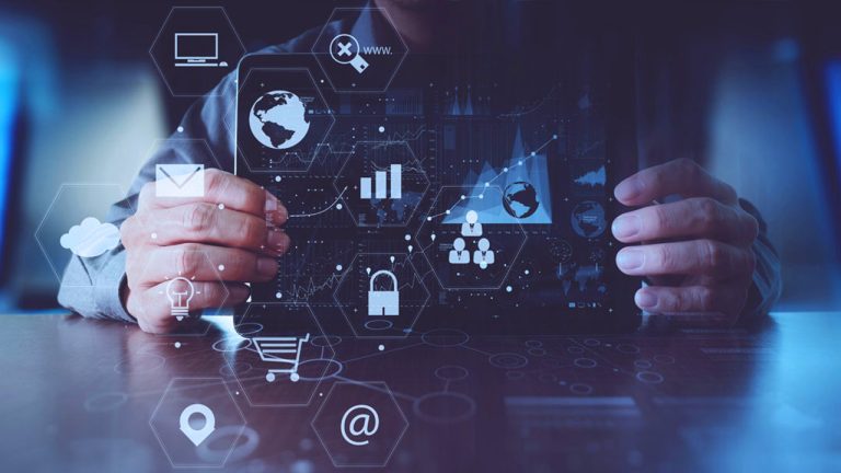 A person holds a transparent digital tablet displaying various icons including a computer, email, cloud storage, globe with connections, bar chart, shopping cart, location pin, lock, and connected people. The background consists of data charts and graphs.