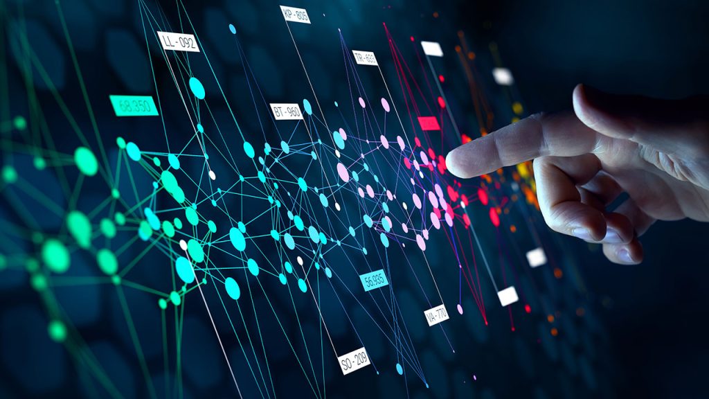 A hand reaches towards a digital interface displaying a complex network of interconnected nodes and lines. The colorful nodes and lines are connected in various patterns, indicating data points and their relationships. The background is dark, enhancing the vibrant visuals.