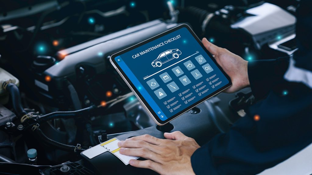 A person holds a tablet displaying a car maintenance checklist over an open car hood. The tablet screen shows various maintenance icons and tasks. Another hand appears to be holding a cloth, possibly for cleaning. The car engine components are visible in the background.