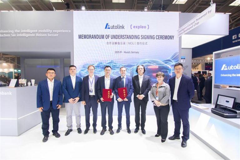 Seven people in business attire stand in front of a display reading "Memorandum of Understanding Signing Ceremony" for Autolink and Expleo. Two hold red folders. The event appears to be in a modern exhibition space.