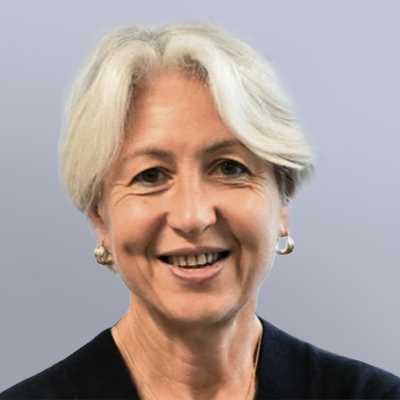 A smiling older woman with short, white hair wearing hoop earrings and a dark top, posed against a plain light gray background.